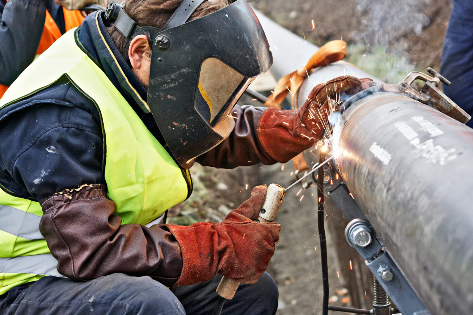 Welder wearing protective clothing for welding industrial construction oil and gas or water and sewerage plumbing pipeline outside on site